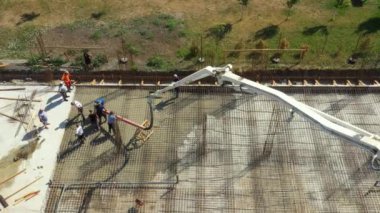 Aerial view construction worker is directing the pump tube as pouring layer of concrete in building foundation. Worker is using power tool, compactor, electric vibratory, compacting fresh concrete.