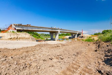 Team of workers are working on the unfinished bridge, road over river is under construction, building site.