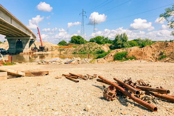 View on a heap of corrosion pipes disassembled steel scaffold joints placed on the ground at the construction site, bridge is in the background.