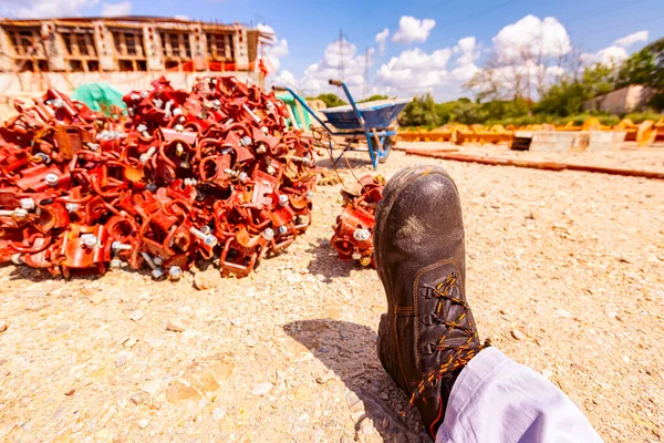 View of a worker\'s safety shoe on a construction site, a pile of disassembled scaffolding parts in the background