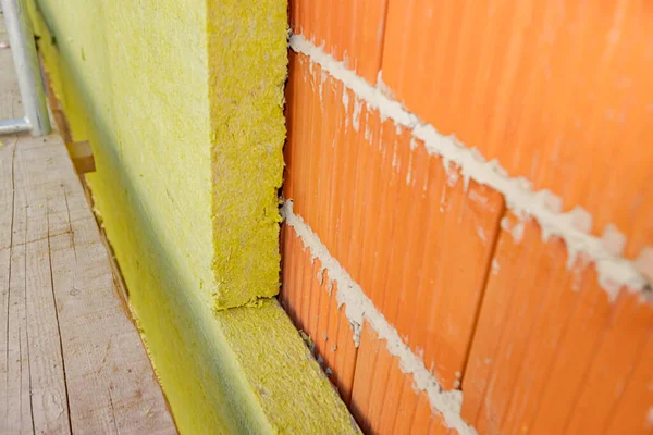 Applying thermal isolation stone wool on the brick wall of residential building under construction. Heat insulation with mineral wool.