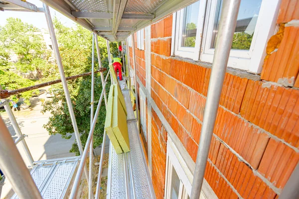 Rock wool panels lined up on scaffolding, waiting for installation, worker installing thermal insulating stone wool on residential building, wall covered with stone wool.