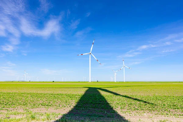 Long shadow under wind generator, turbines, with rotating blades, propellers, renewable clean energy converting kinetic energy.