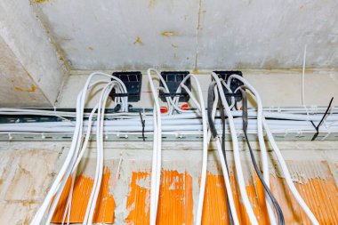 İnşaat halindeki binanın tavanından kablolar sarkıyor. Elektrik kablolarının ve kablolarının yerleştirilmesi.