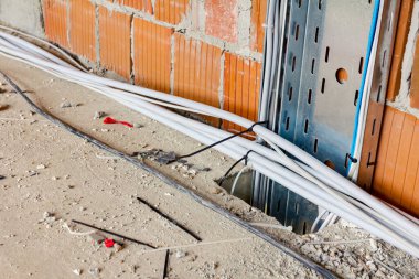 Yalıtımlı kablolarla dolu metal delikli tepsi inşaat halindeki bir binanın zemininde ikinci dereceden bir delikten geçiyor..
