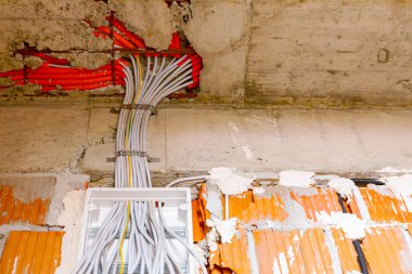 Çeşitli kablolar duvara monte edilmiş plastik bir sigorta kutusundan sarkıyor, bina yapım aşamasında, devam ediyor. Elektrik kablolarının ve kablolarının kurulumu.