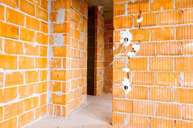 Duvardaki kabloların montajı için üst kapakları sökülmüş prizler ve inşaat halindeki bina blokları..