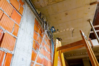 Kablolar için merdivenler, elektrik için dağıtım kutuları. Bir grup kablo tavandan sarkıyor, inşaat halindeki katların arasından geçiyor..