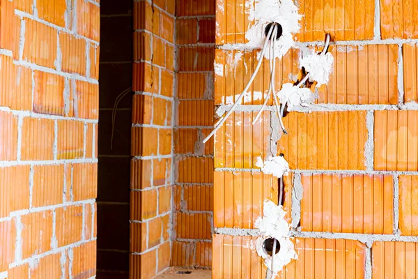 Exposed electrical sockets with the top covers removed for installation of the wiring on the wall with blocks of building under construction.