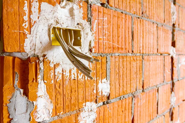 Cables are hanging from junction box placed on the wall of building under construction, work in progress. Placement of electrical wires and cables.