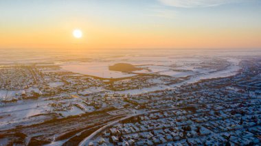 Hava manzarası evlerin çatılarında kardan beyaz, gökyüzünde güzel bir gün batımı, kışın soğuk şehir manzarası.  