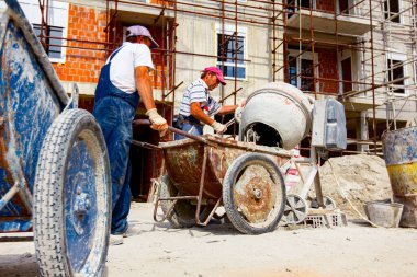İşçiler taşıması için vinç kancalarına bağlı el arabalarına havan topu dökerler..