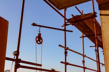 Paslı demir endüstriyel makara iskeleye bağlı halatla kargoyu kaldırmaya yerleştirildi, mavi gökyüzü arka planda..