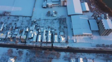 Yukarıda, doli hareket ediyor, endüstriyel kompleksin üzerine doğru eğiliyor, birkaç silo ve büyük depolar, beyaz karla kaplı, kış.