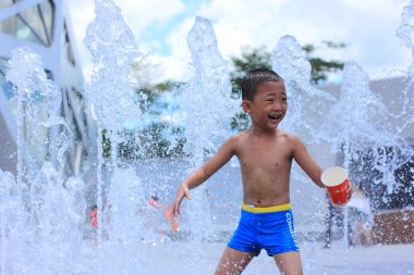 Asyalı çocuk su çeşme tarafından yaz aylarında sıçrayan.