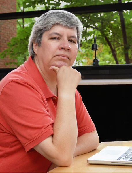 Middle-aged woman at laptop, looking at you — Stock Photo, Image