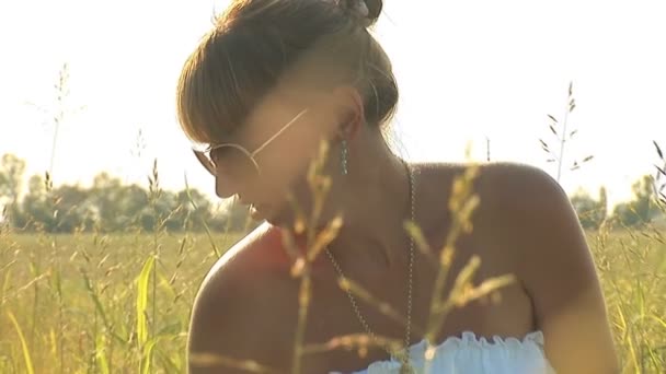 Mujer de blanco en un prado verde con gafas de sol — Vídeo de stock