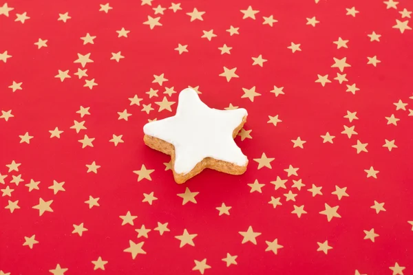 Biscoito de canela em forma de estrela no fundo vermelho com estrelas douradas — Fotografia de Stock