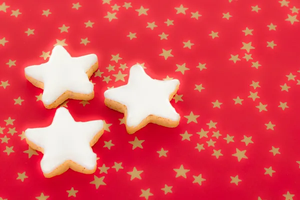 Shining star shaped cinnamon biscuits on red background with golden stars — Stock Photo, Image