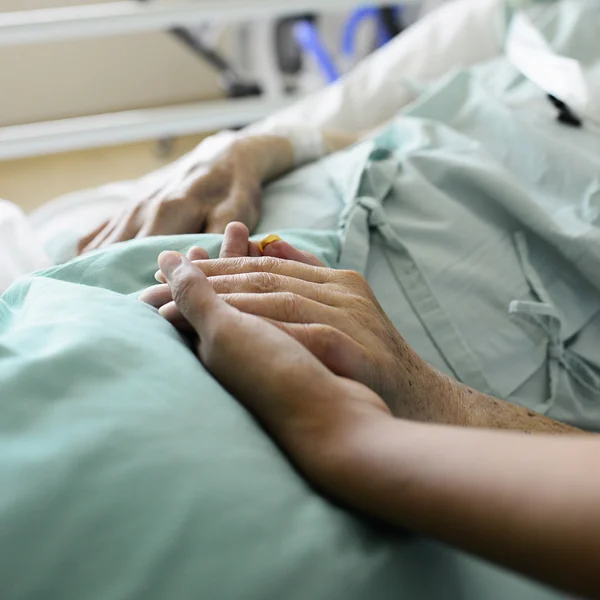 Uma jovem mão toca e segura uma velha mão enrugada no hospital — Fotografia de Stock