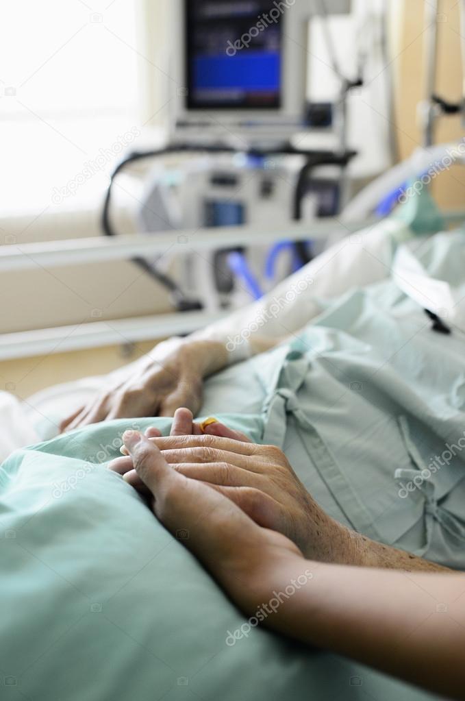 A young hand touches and holds an old wrinkled hand in hospital