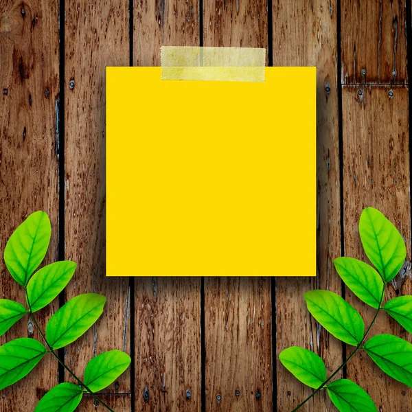 Nota de papel amarillo y hojas verdes sobre el fondo de madera viejo — Foto de Stock