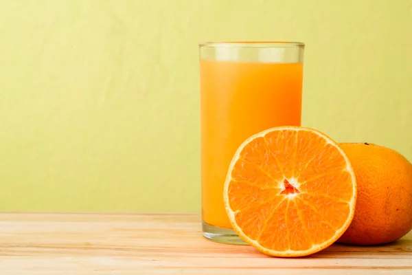 Frischer Orangensaft auf Holztisch vor gelbem Hintergrund — Stockfoto