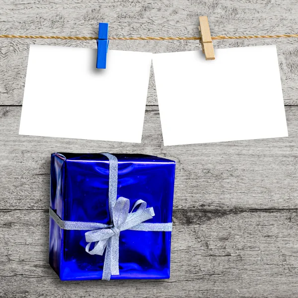 Blue gift box on wooden wall with a blank paper hanged — Stock Photo, Image