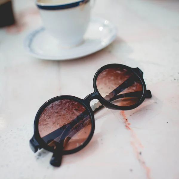 bir fincan kahve ile mermer masa üzerinde güneş gözlüğü.