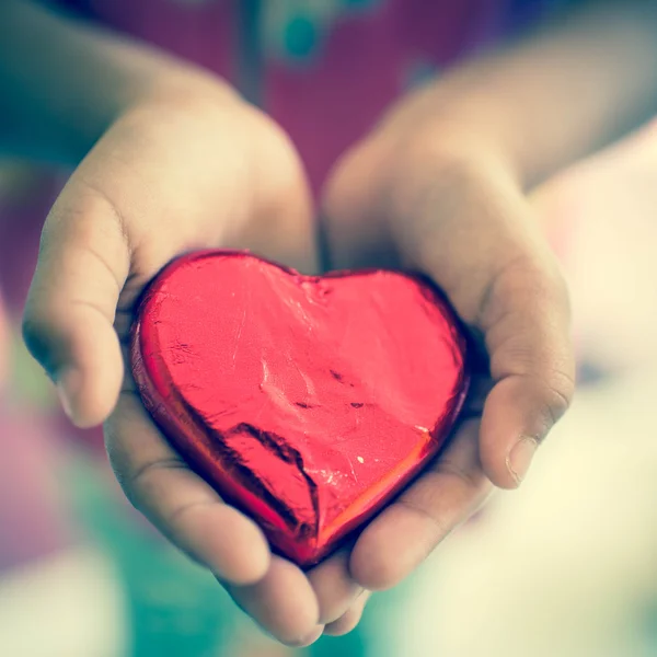 Corazón de caramelo envuelto en papel de aluminio rojo en las manos del niño —  Fotos de Stock