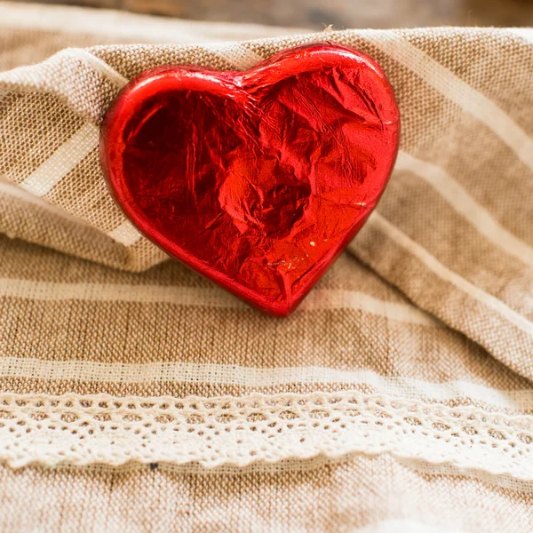 Corazón de caramelo envuelto en lámina roja sobre fondo de tela de textura marrón —  Fotos de Stock