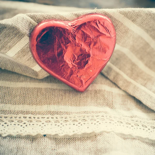 Corazón de caramelo envuelto en lámina roja sobre fondo de tela de textura marrón —  Fotos de Stock