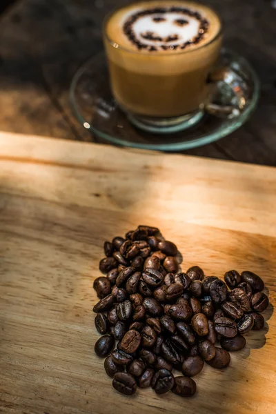 Hjärta form av kaffebönor och en kopp kaffe på trä bakgrunds — Stockfoto