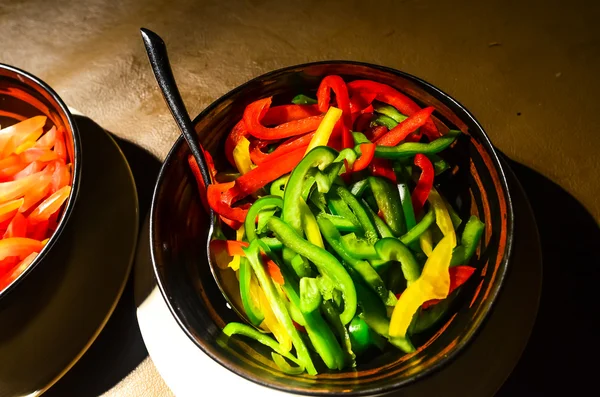 Red yellow and green bell peppers, sliced in black bowl, still l — Stock Photo, Image