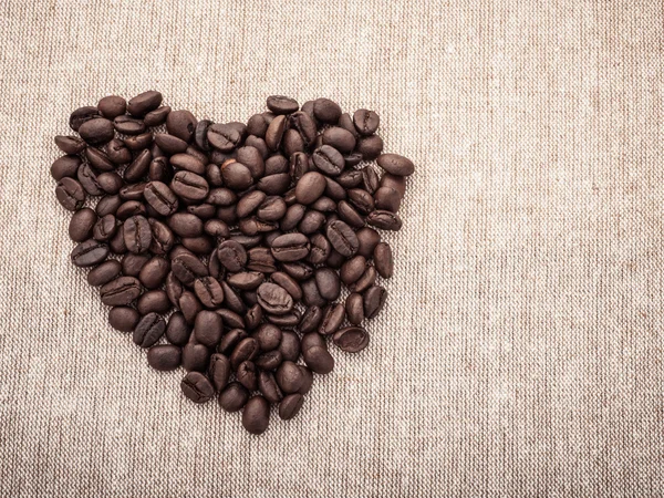 Coffee Beans with heart shape on brown fabric — Stock Photo, Image