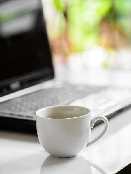 Taza de café y computadora portátil para negocios, enfoque selectivo en el café . — Foto de Stock