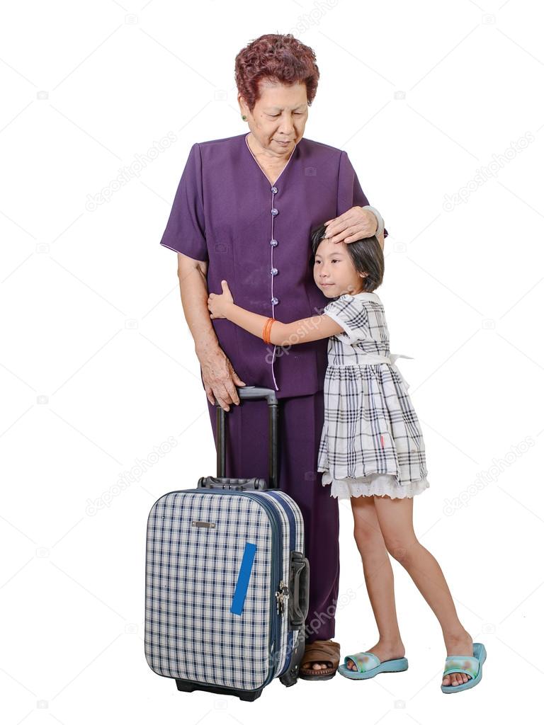 Senior woman hugging crying girl with suitcase.
