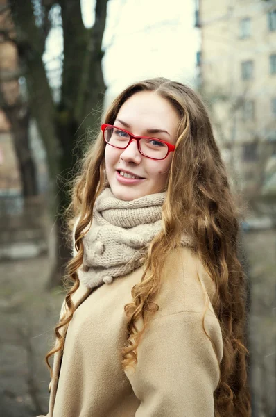 Jeune fille dans des lunettes rouges et manteau avec de longs cheveux bouclés rouges Photo De Stock