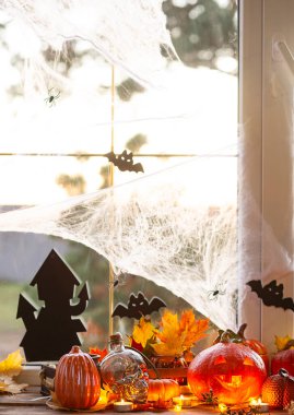 Cadılar Bayramı için pencere kenarındaki evin şenlikli dekoru - balkabakları, fenerler, kafatasları, yarasalar, örümcek ağları, mumlar ve bir çelenk - rahat ve korkunç bir atmosfer