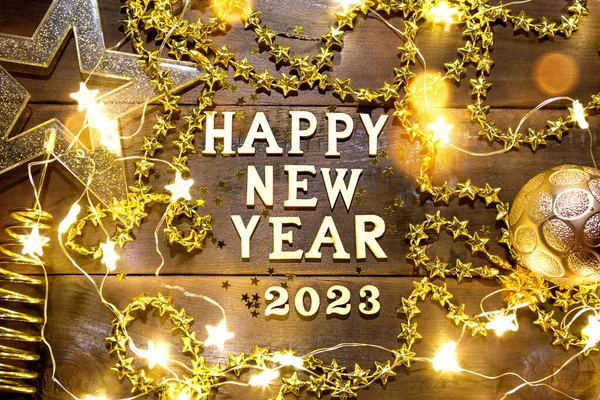 Mutlu yeni yıl ahşap harfleri ve pulları, yıldızları, parıltıları, çelenk ışıkları olan şenlikli bir arka planda 2023 numaraları. Selamlar, kartpostal. Takvim, kapak