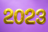 Šťastný Nový rok - zlatá čísla 2023 na purpurovém pozadí s flitry, hvězdami, třpytkami, světly věnců. Zdravím, pohlednice. Kalendář, obal. 