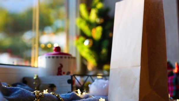 手がピックアップし クリスマスの装飾でテーブルの上に食品配達サービスのパッケージを置きます 環境に優しいリサイクル可能なパッケージ ホリデーケータリング デザート クッキー お菓子の家を作る モックアップ — ストック動画