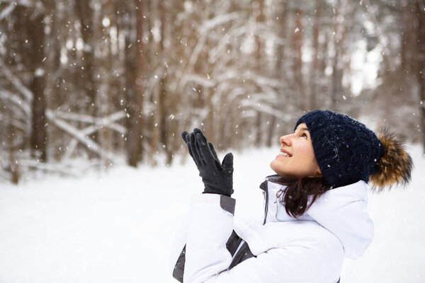 Женщина в тёплой вязаной шляпе закрыла глаза улыбкой и наслаждается снегом, холодной погодой. Активный отдых на свежем воздухе, сезон, зима, тает снег. Покрытый морозом, красивая улыбка. Портрет крупного плана
