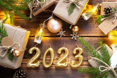 Ahşap arka planda mumlar, hediye kutuları ve çevre dostu Noel dekorları olan 2023 model mumlar. Sahte etiketler, doğal dekor, koniler, iğneler. Şenlik havası. Açıkça, yeni yıl arkaplanı