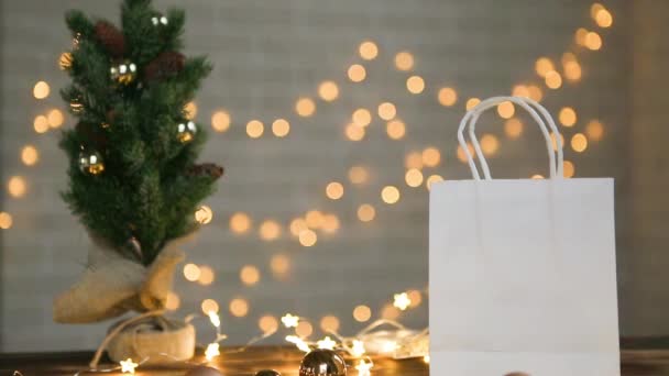 手でピックアップし テーブルの上から注文を入れます クリスマスツリーと妖精の光の近くにクリスマスと新年のための贈り物と紙袋 リサイクル可能なパッケージ 廃棄物ゼロ — ストック動画