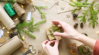 Eller Noel ve yeni yıl hediyelerini çevre dostu malzemelerle paketliyor: Kraft kağıdı, canlı köknar dalları, koniler, sicim, yayla bağlanmış. Sahte etiketler, doğal dekor, el yapımı, düz. Şenlik havası