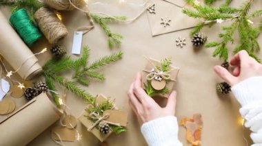 Eller Noel ve yeni yıl hediyelerini çevre dostu malzemelerle paketliyor: Kraft kağıdı, canlı köknar dalları, koniler, sicim, yayla bağlanmış. Sahte etiketler, doğal dekor, el yapımı, düz. Şenlik havası