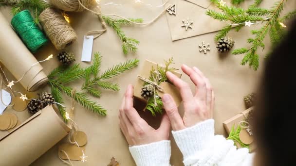 手は環境に優しい材料でクリスマスと新年のための贈り物をパック クラフト紙 ライブモミの枝 コーン ツイン 弓で縛ら モックアップ付きタグ 自然装飾 手で作られ フラットです — ストック動画