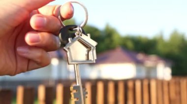 Anahtarlığı elinde anahtarlık olan anahtarlık. Çitlerin ve kulübenin arka planı. Yeni bir eve taşınmak, ipotek, emlak almak, konut kiralamak ve rezervasyon, köyde yaşama hayali. Boşluğu kopyala