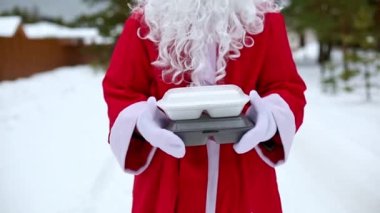 Noel Baba 'nın ellerinde karlı havada yiyecek dağıtım konteynırları. Noel arifesi terfisi. Hazır sıcak sipariş, tek kullanımlık plastik kutu. Yeni yıl yemekleri. Uzayı kopyala, taklit et